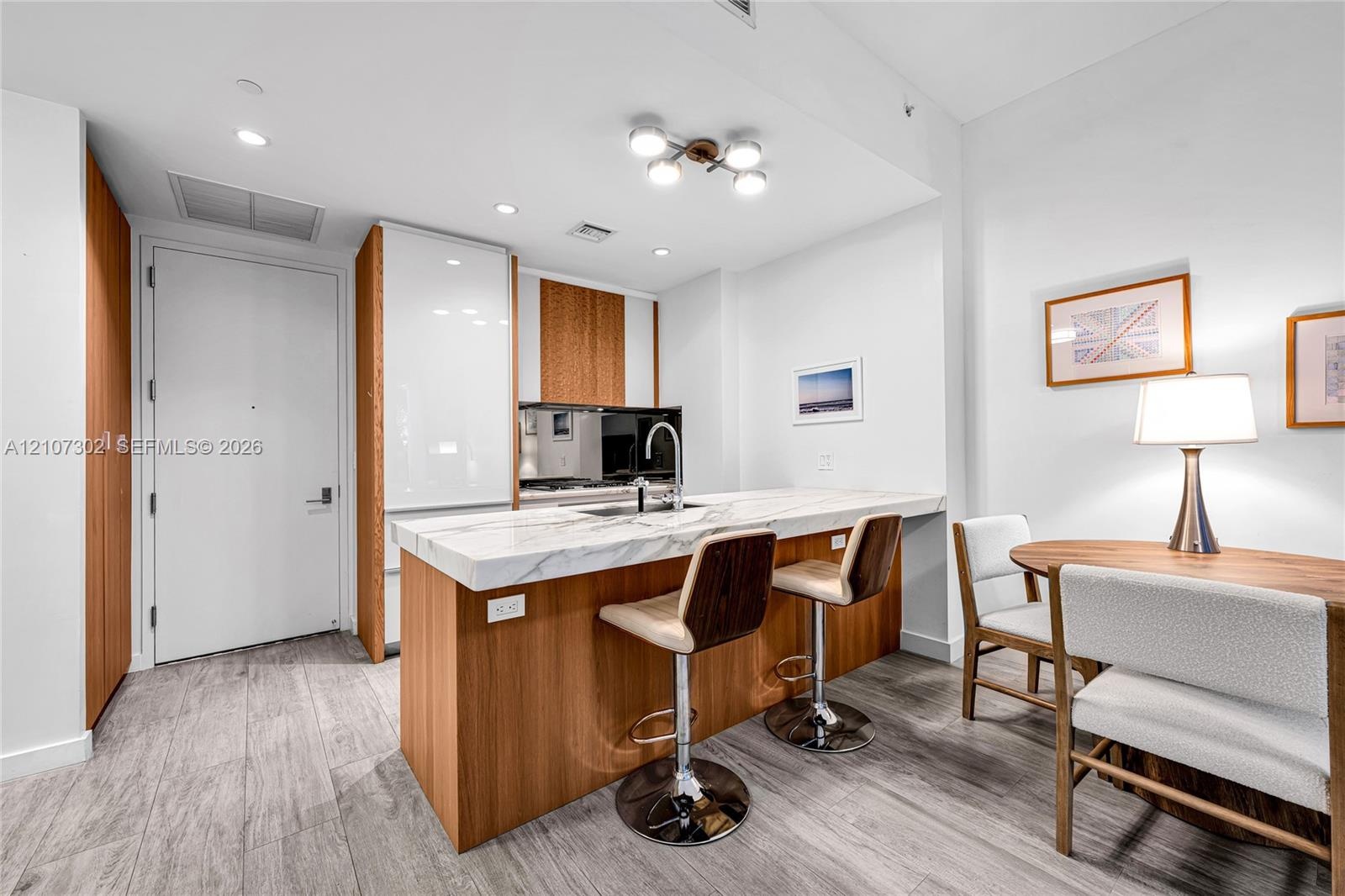 Kitchen featuring wood-finish cabinetry, white high-gloss paneling, integrated refrigerator, stone-composite countertop with waterfall edge, and wood-