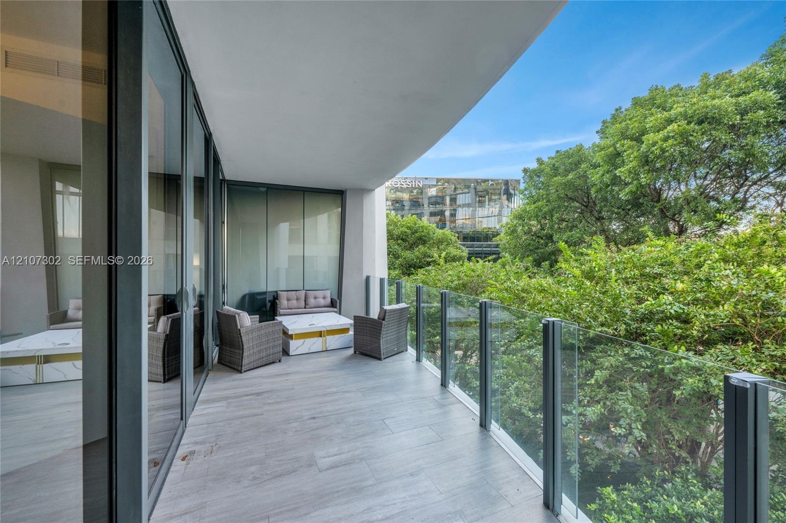 Covered balcony featuring wood-finish flooring, floor-to-ceiling glass doors, and a frameless glass railing system