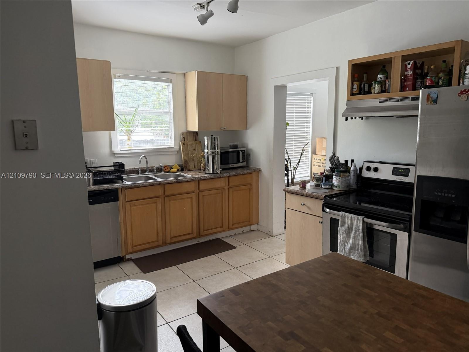 Kitchen featuring cabinetry with light-finish wood doors, stone-finish countertops, ceramic tile flooring, and integrated stainless steel appliances