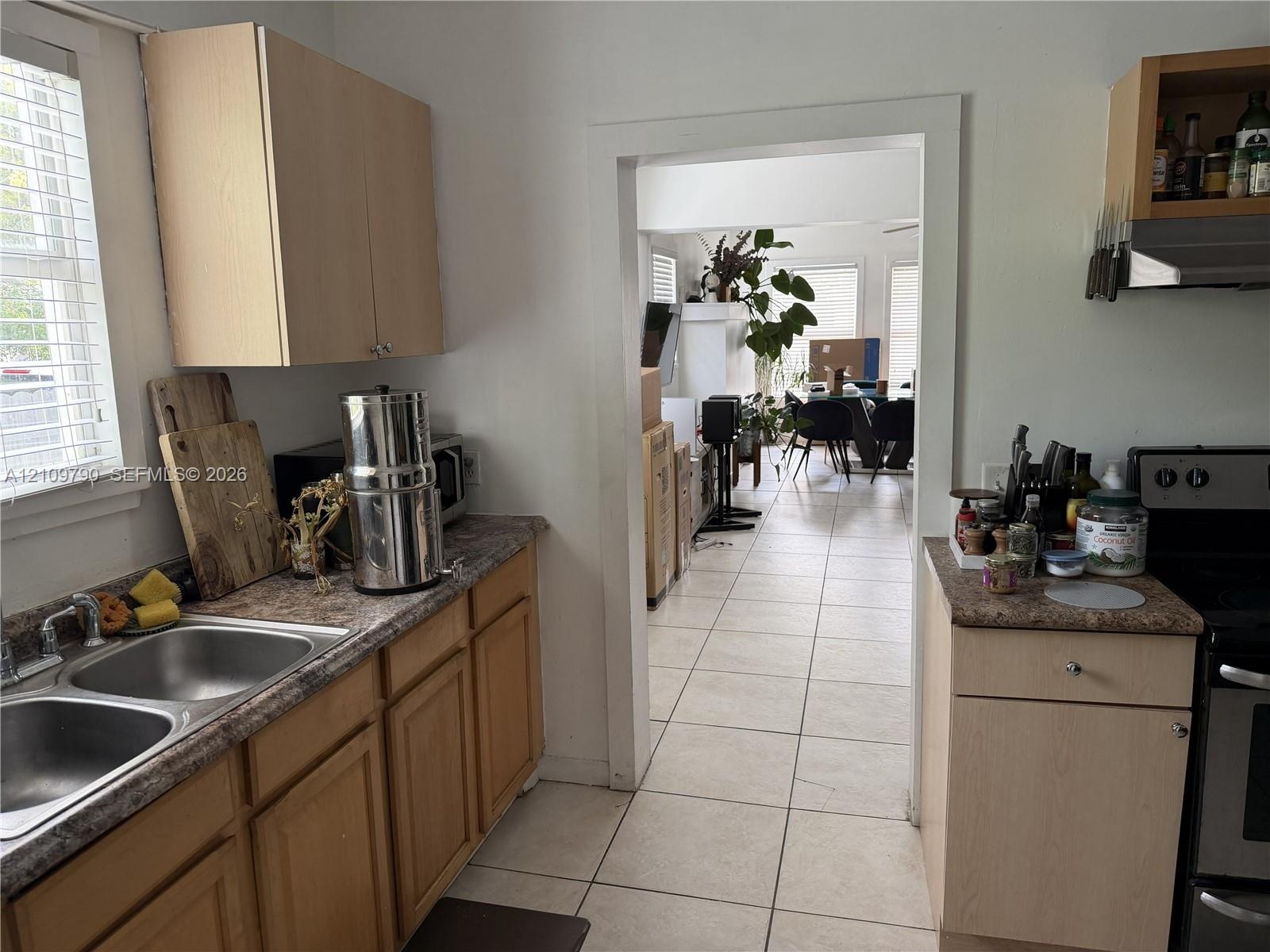 Kitchen featuring light wood-finish cabinetry, laminate countertops, a double-basin stainless steel sink, and ceramic tile flooring