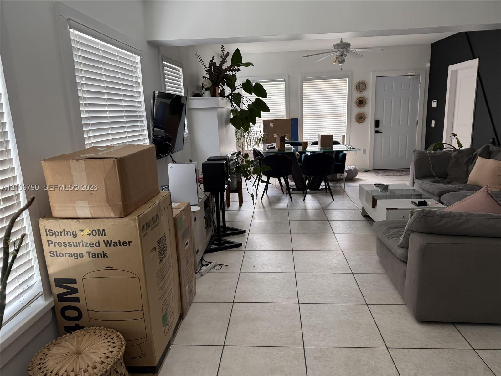 Open-concept interior featuring neutral ceramic tile flooring, oversized multi-pane windows, and a ceiling-mounted fan