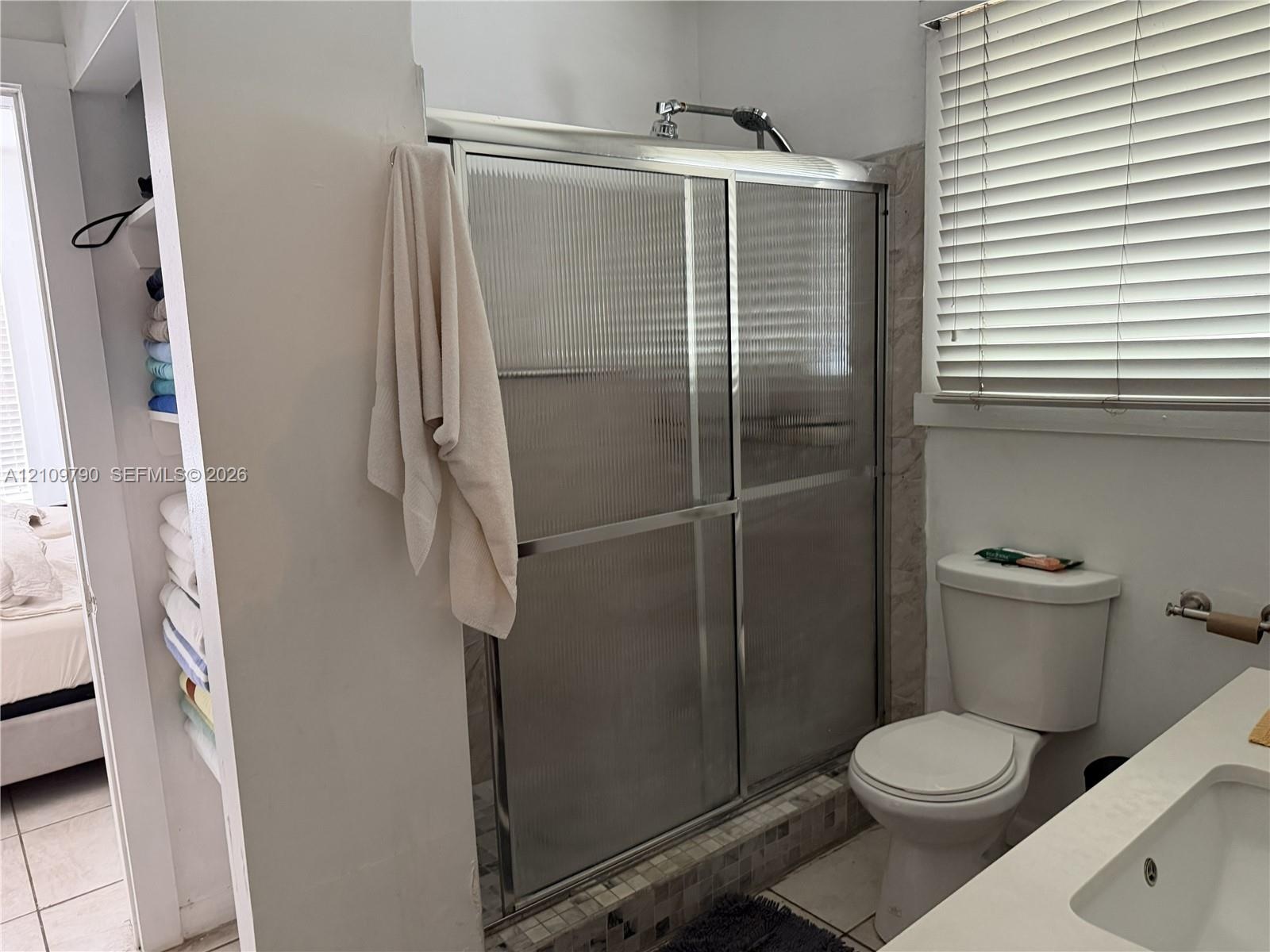 Shower enclosure featuring a chrome-frame sliding door, walk-in design with a tiled threshold, built-in recessed shelving, two-piece toilet, and vanit