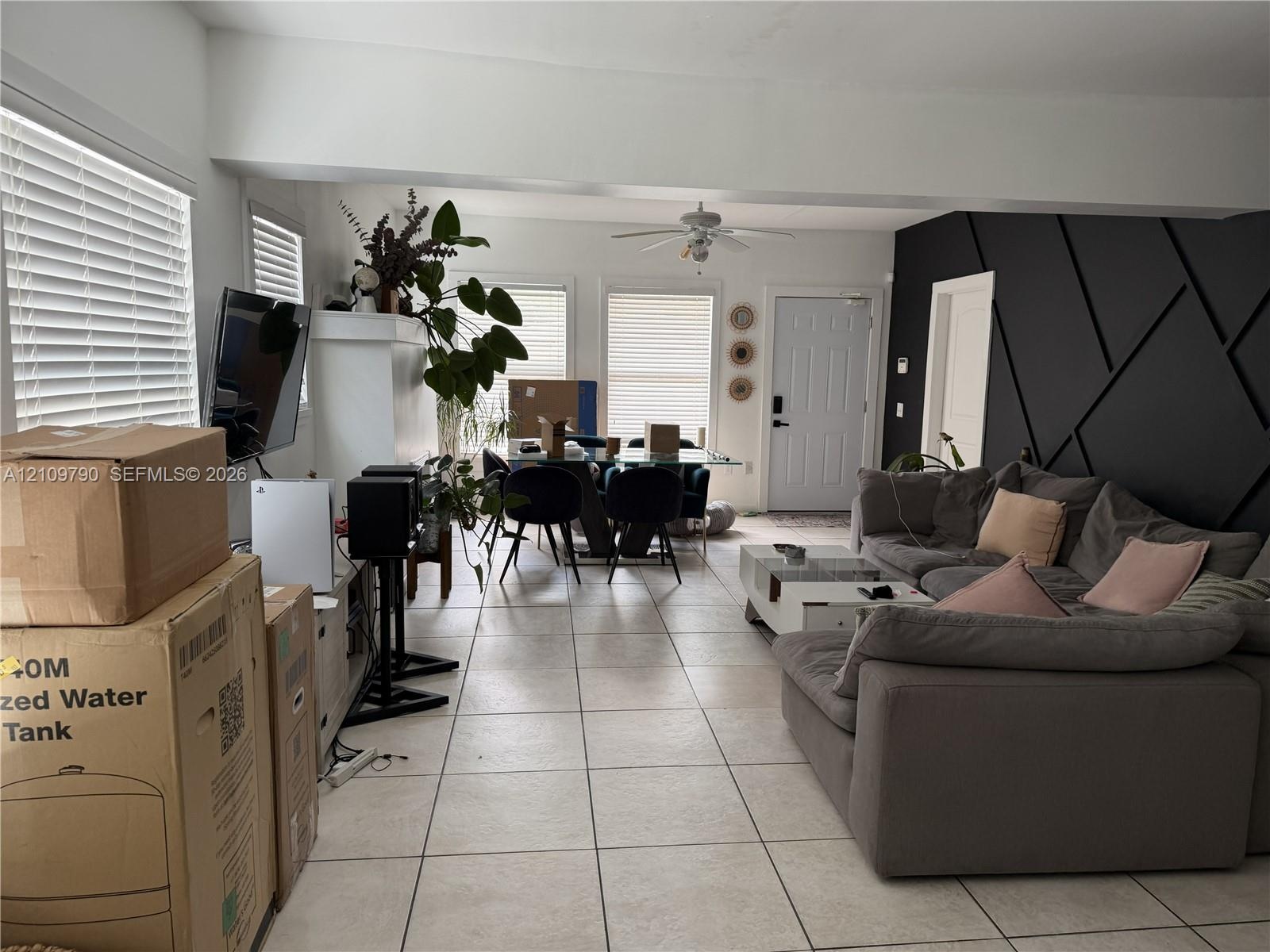 Open-concept interior featuring large-format tile flooring, matte black geometric wall paneling, multiple windows with horizontal blinds, and a ceilin