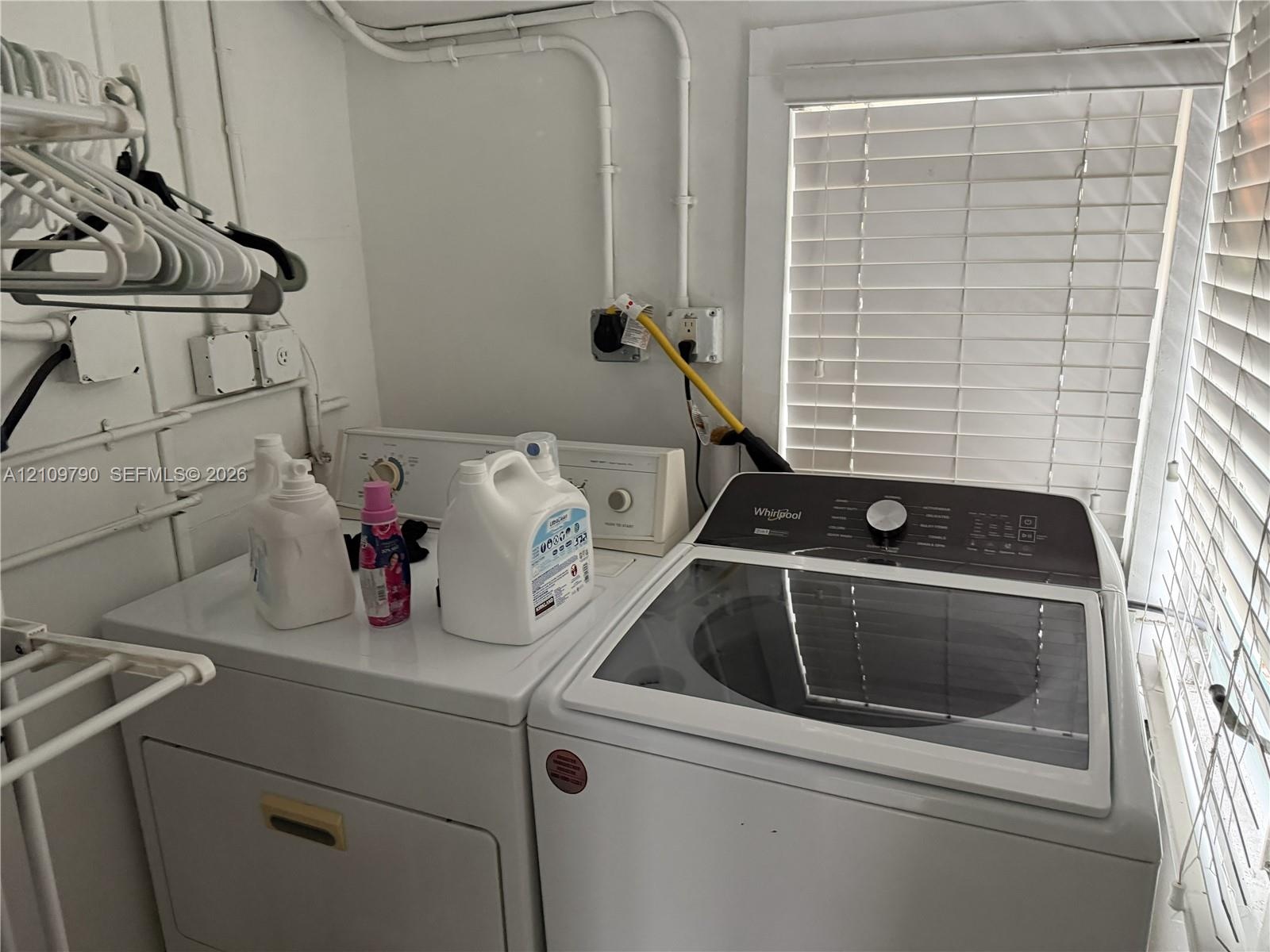 Dedicated laundry area featuring a top-load washer, a built-in dryer, white wall-mounted garment rack, and horizontal slat window blinds
