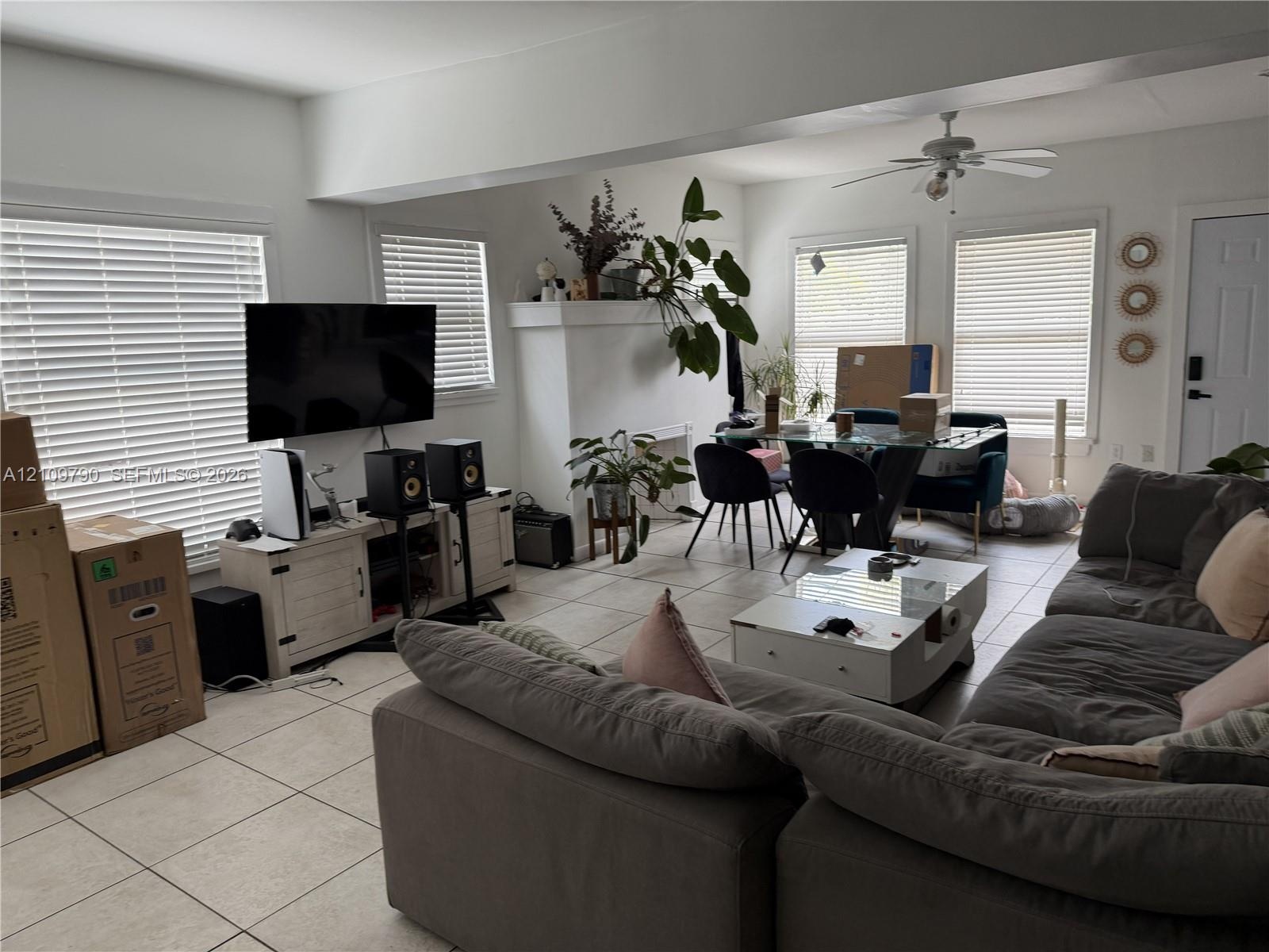 Living area featuring large format neutral tile flooring, neutral wall tones, multiple windows with integrated blinds, a central ceiling fan, and a pr