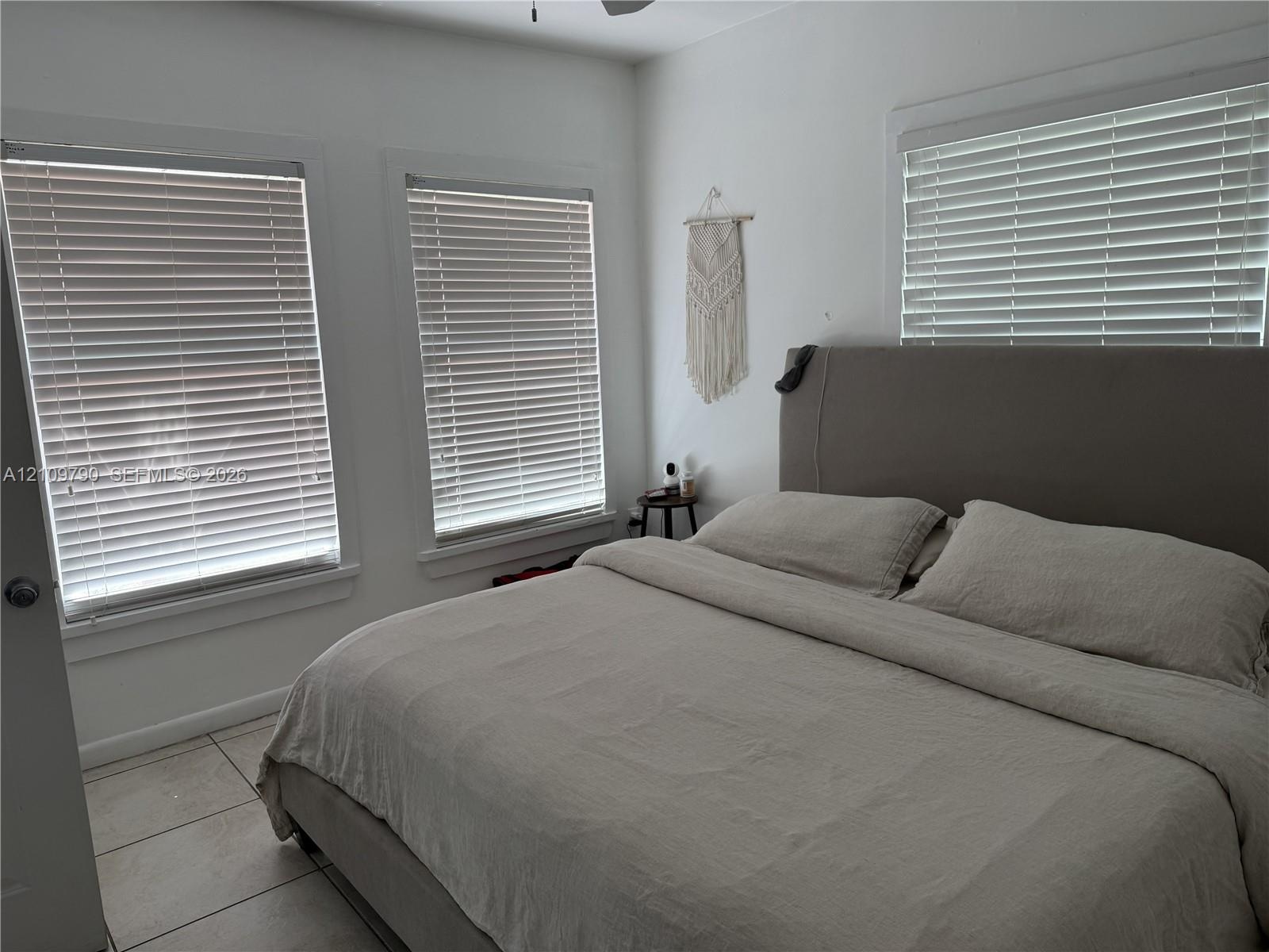 Neutral-toned room featuring light-colored tile flooring, triple windows with horizontal blinds, and a ceiling fan