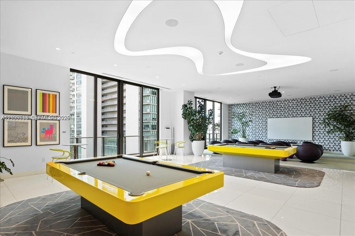 Expansive recreational room featuring custom curvilinear recessed ceiling lighting, full-height glass doors, large-format tile flooring, and a pattern
