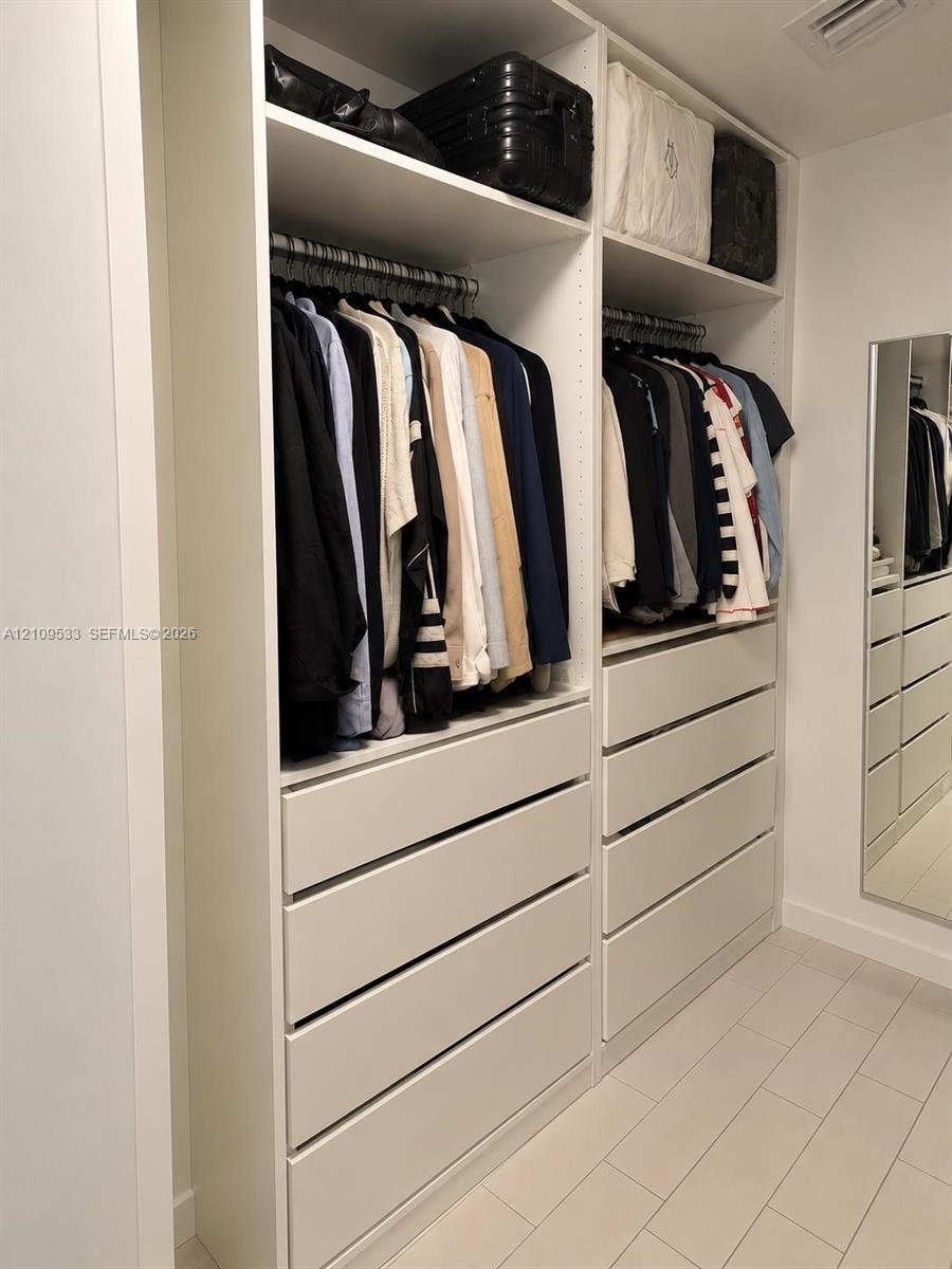 Custom floor-to-ceiling cabinetry with integrated hanging rods, extensive drawer storage, overhead shelving, and an inset full-length wall mirror