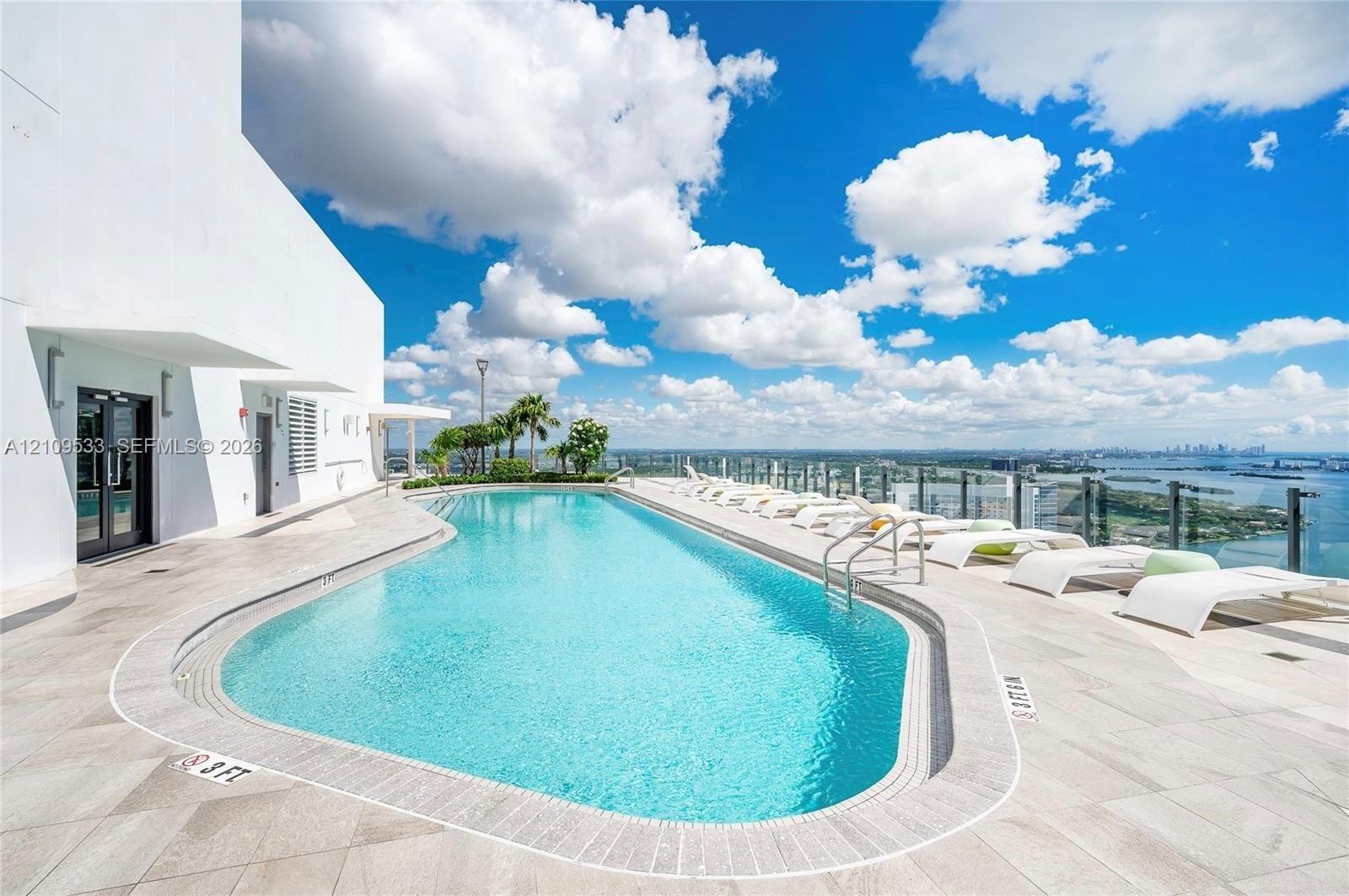 Rooftop pool featuring light-toned stone tile decking, a glass panel perimeter railing, and concrete structural elements