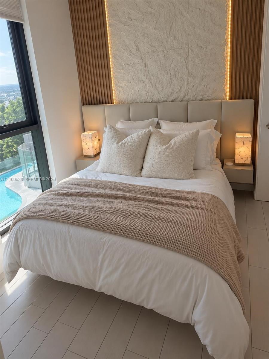 Floor-to-ceiling windows, vertical wood-slat wall paneling, integrated stone accent wall, light-toned tile flooring, and wall-mounted bedside cabinetr
