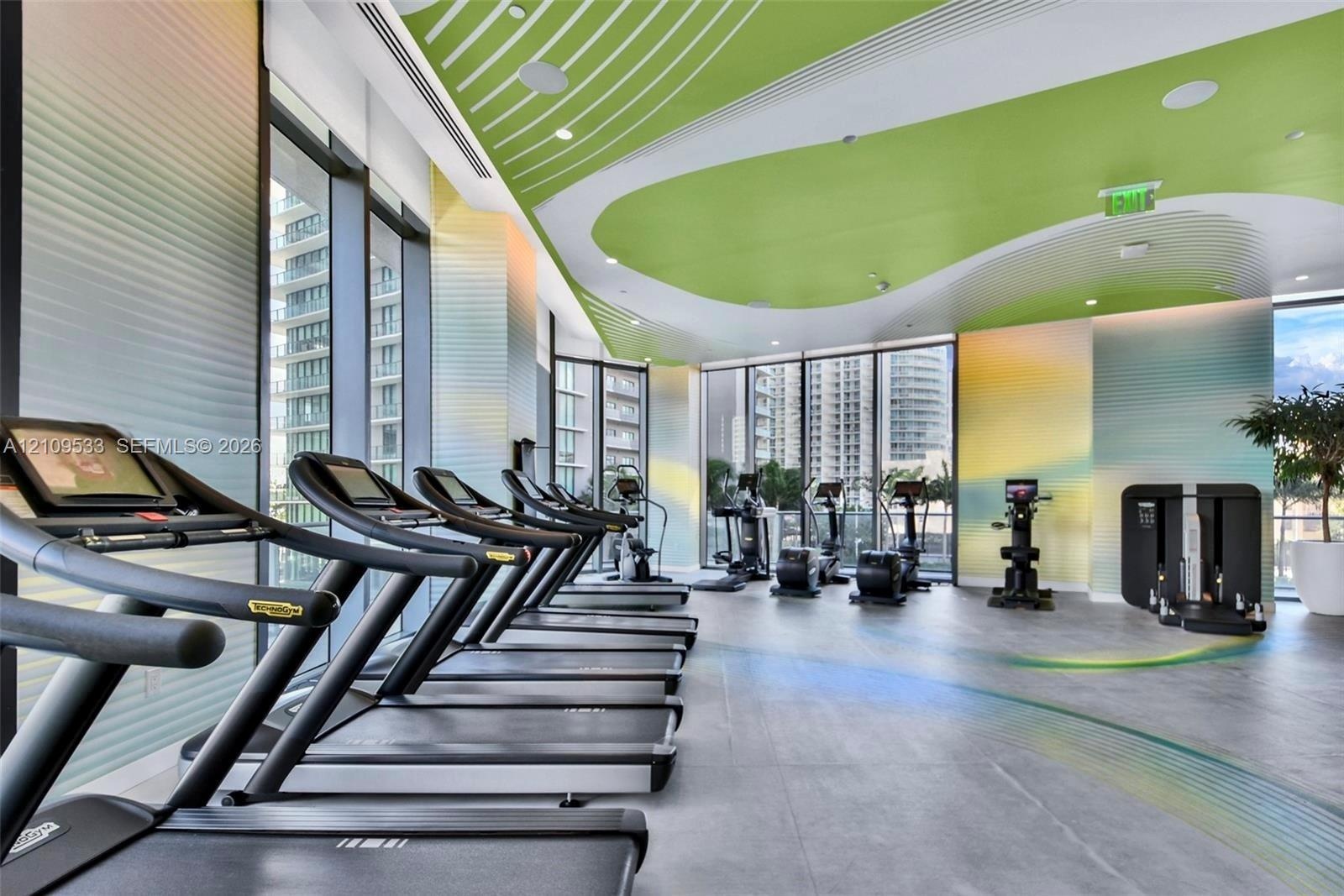 Fitness facility featuring floor-to-ceiling windows, large-format tile flooring, a custom curvilinear acoustic ceiling design, and integrated recessed