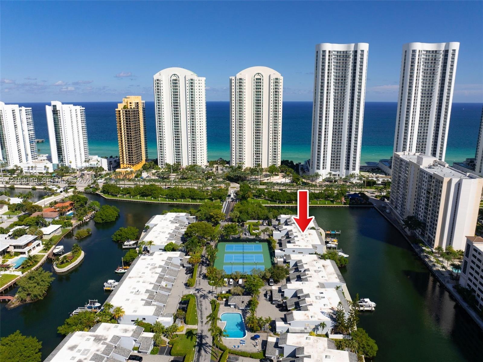Aerial perspective of a multi-unit property complex featuring tennis courts, a swimming pool, and direct canal access