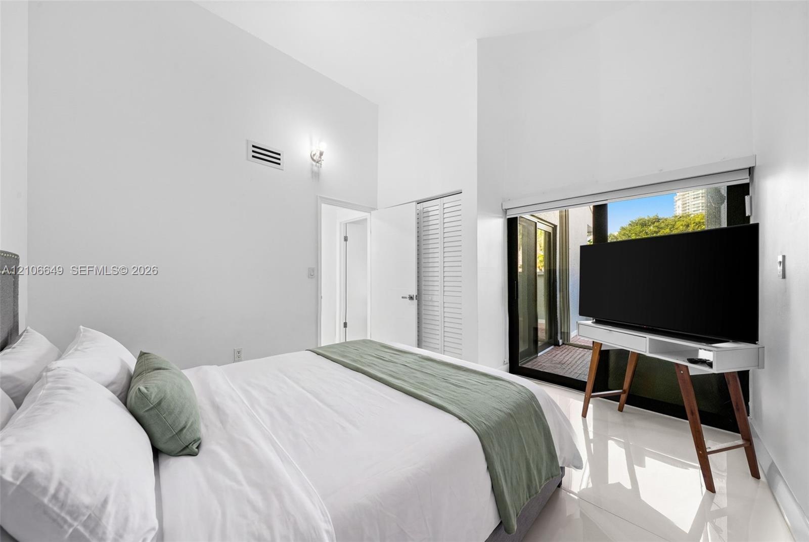 Vaulted ceilings, large sliding glass doors, white tiled flooring, and louvered closet doors