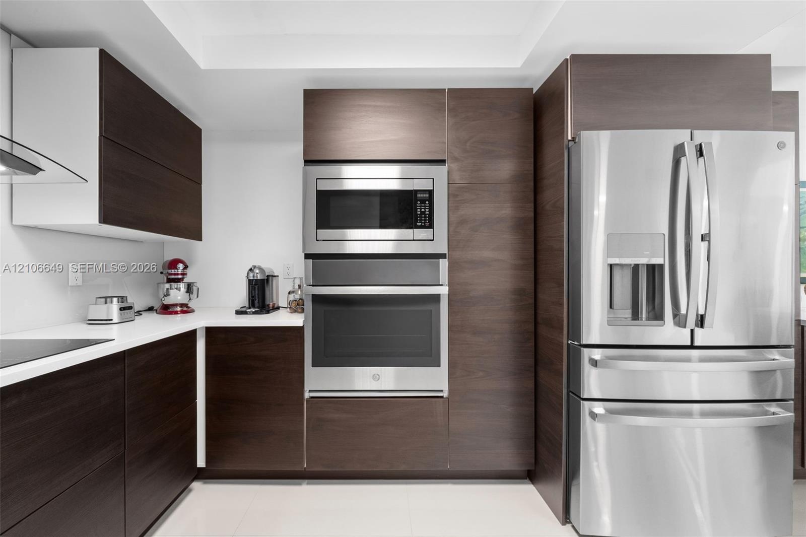 Modern kitchen featuring dark wood-finish cabinetry, solid surface countertops, stainless steel wall oven, built-in microwave, and stainless steel fre