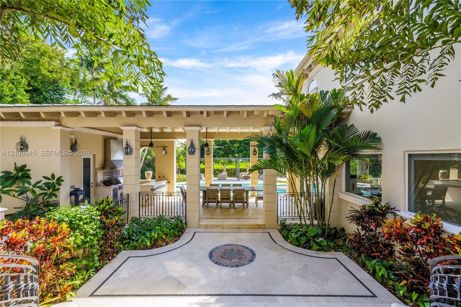 Covered lanai featuring a stone-paver patio with decorative inlay, built-in outdoor kitchen with stainless steel ventilation hood, and heavy-timber be