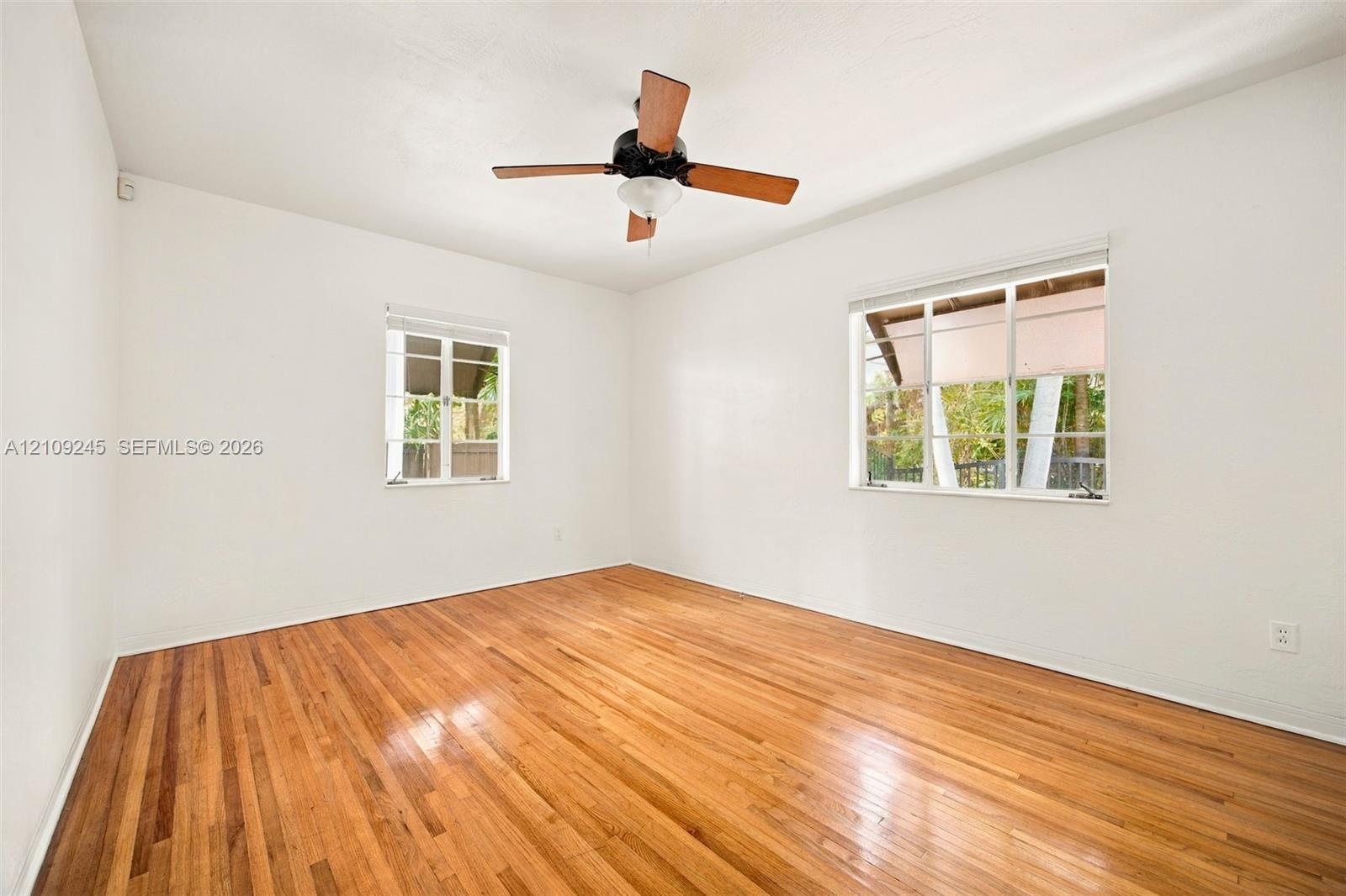 Room featuring wood-finish flooring, multi-pane windows, and a ceiling fan with integrated lighting