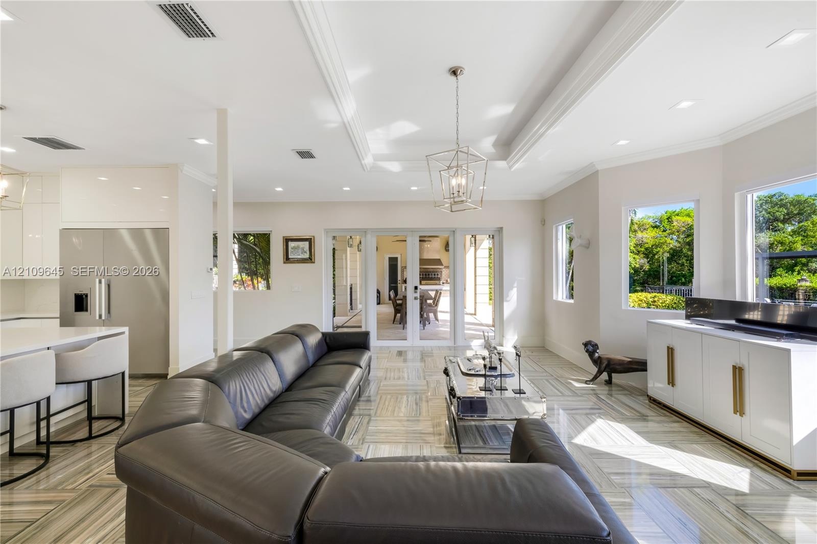 Open-concept living space featuring high ceilings with crown molding, recessed lighting, geometric metal pendant fixture, large-format tile flooring, 