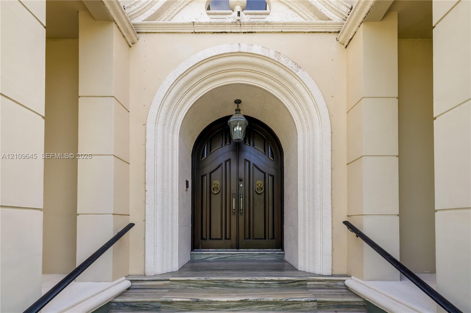 Double arched solid wood doors featuring brass lion-head knockers, set within a recessed masonry entryway with decorative molding, stone-stepped riser
