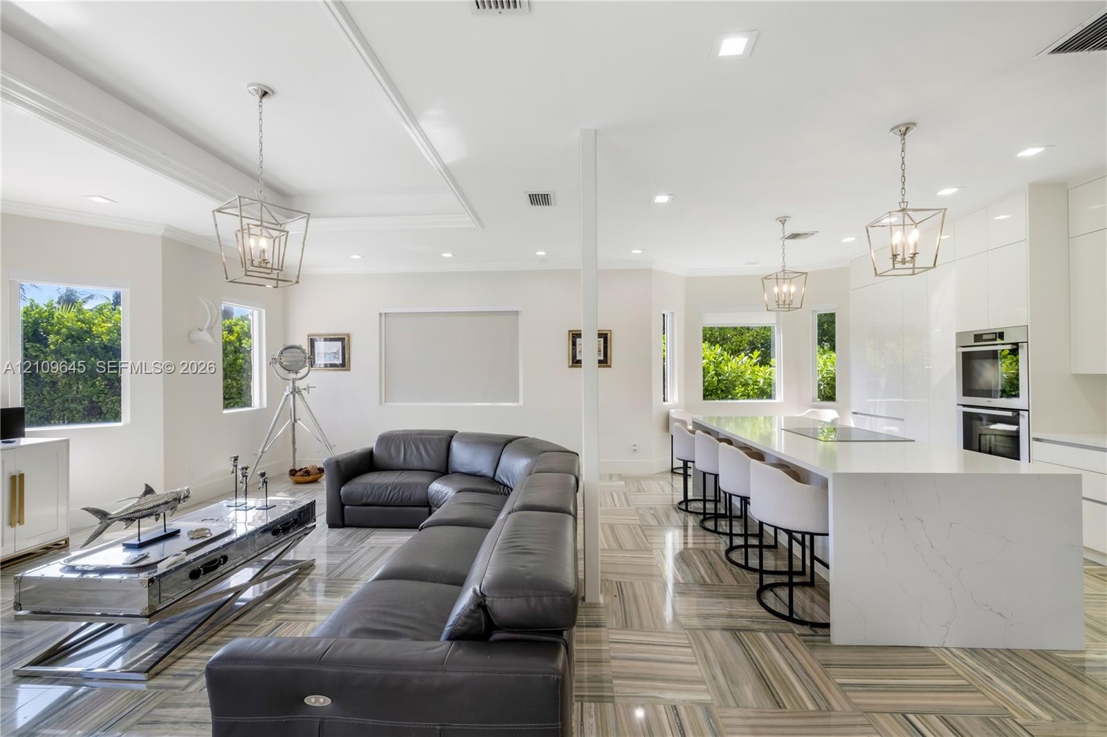 Open-concept interior featuring large-format tile flooring, a waterfall-edge stone island with integrated cooktop, dual built-in wall ovens, recessed 
