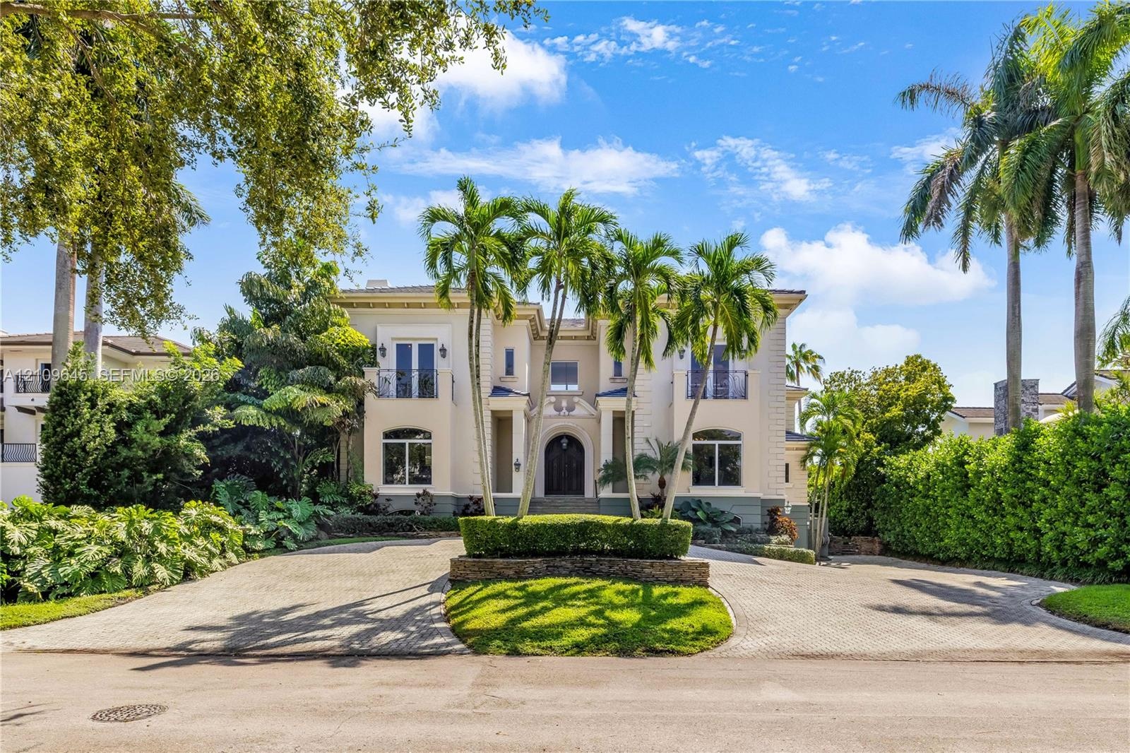 Two-story Mediterranean-style exterior featuring a stucco facade, arched entryway, upper-level balconies with wrought-iron railings, and a circular pa