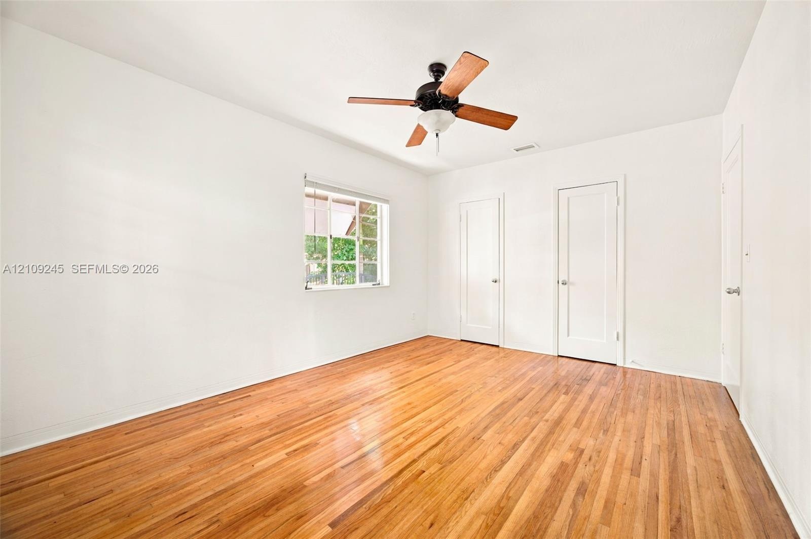 Room featuring wood-finish flooring, a multi-pane window, and a ceiling-mounted light fixture with a fan