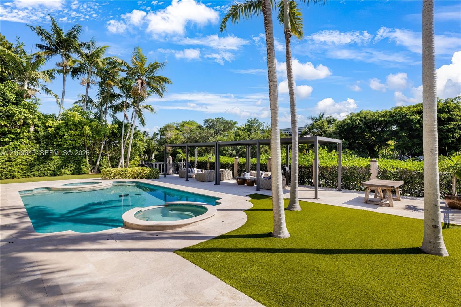 Backyard featuring an in-ground swimming pool, attached spa, stone-finish pool deck, synthetic turf lawn, and metal-frame pergola