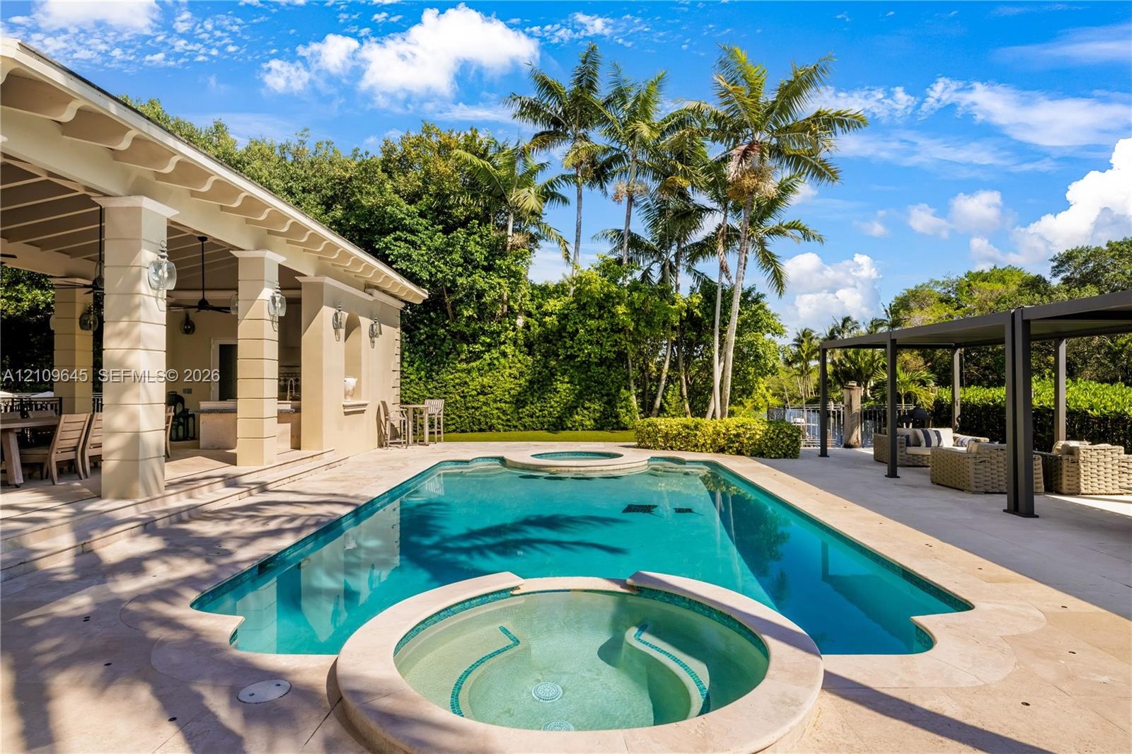 Swimming pool with integrated spa, covered lanai featuring structural columns, paver decking, and metal pergola