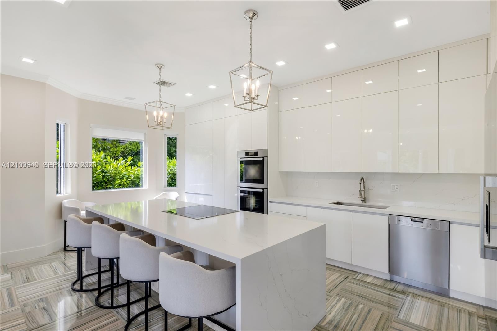 Modern kitchen featuring high-gloss cabinetry, stone-finish countertops, an oversized center island, built-in stainless steel appliances, and patterne