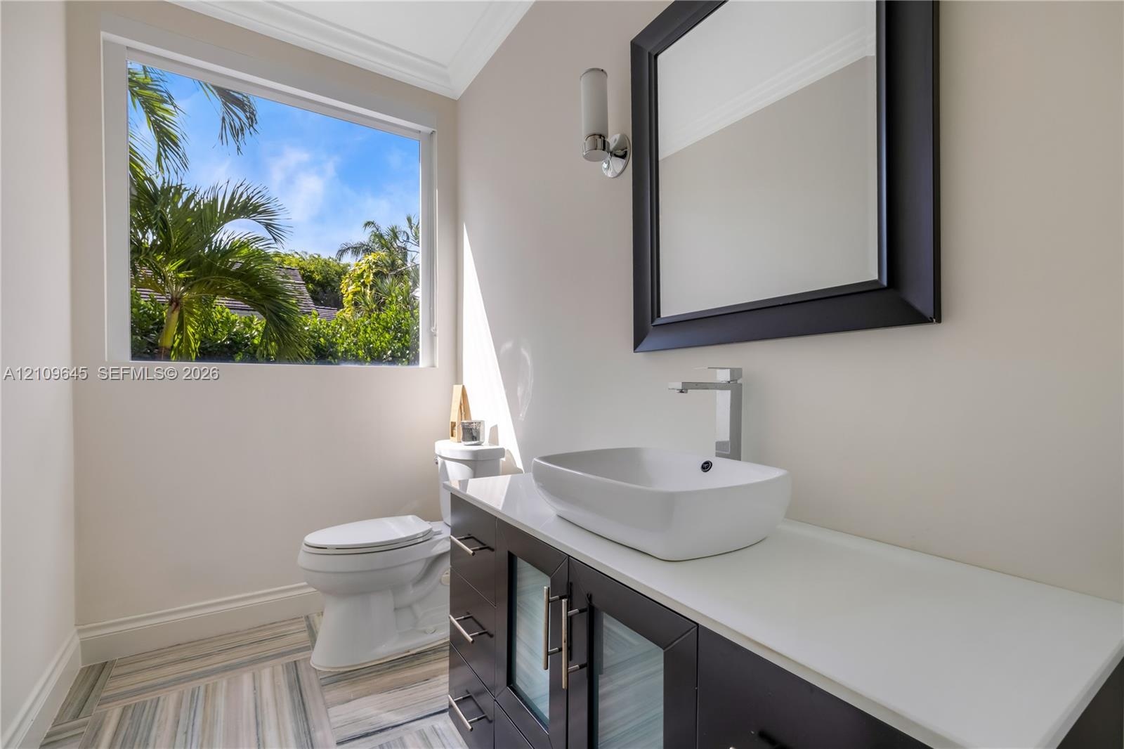 Modern vanity featuring a stone countertop, vessel sink, and metallic hardware, complemented by patterned tile flooring and a wall-mounted light fixtu