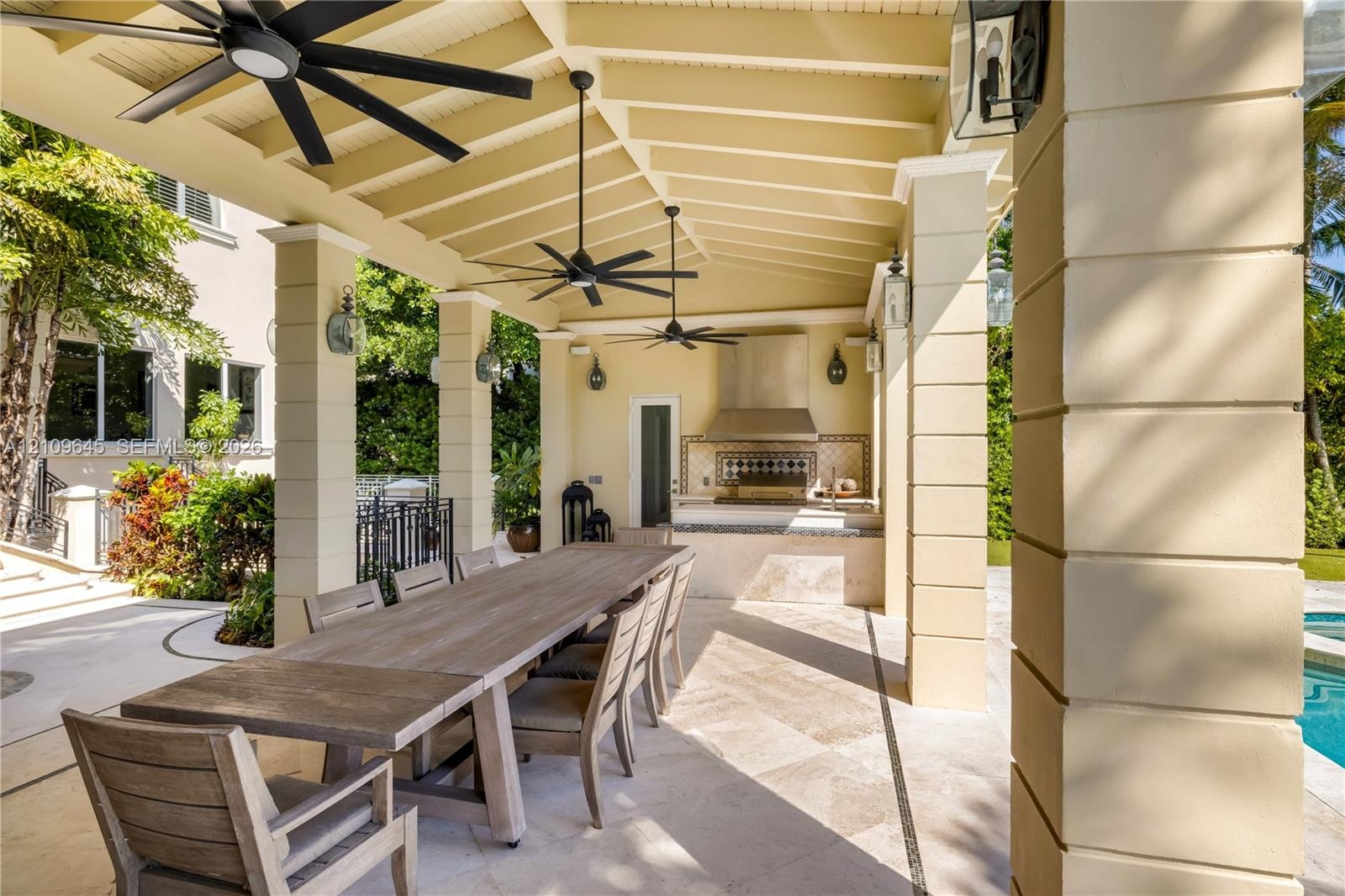Covered outdoor kitchen and dining area featuring a stone-tile patio, built-in stainless steel range hood, stone-clad counter, multi-blade ceiling fan