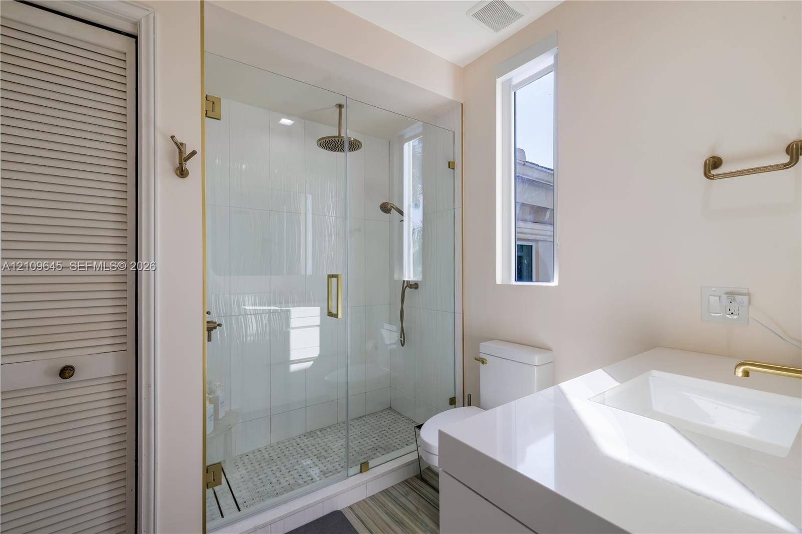 Walk-in glass shower featuring a rain-style showerhead and handheld sprayer with brass hardware, complemented by a white vanity with a rectangular int