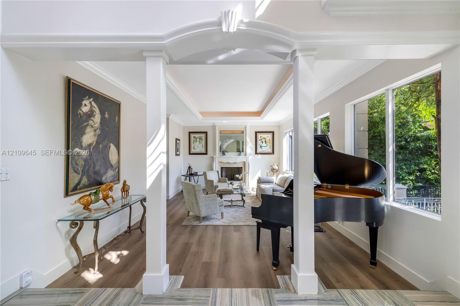 Open floor plan featuring wood-finish flooring, tray ceilings, a central stone-surround fireplace, and large picture windows