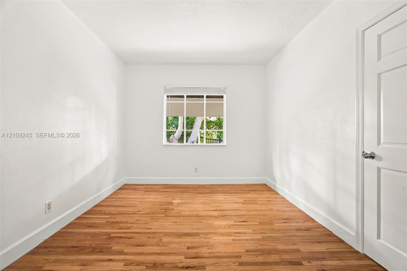 Interior room featuring wood-finish flooring, white walls, and a multi-pane window with a neutral roller shade