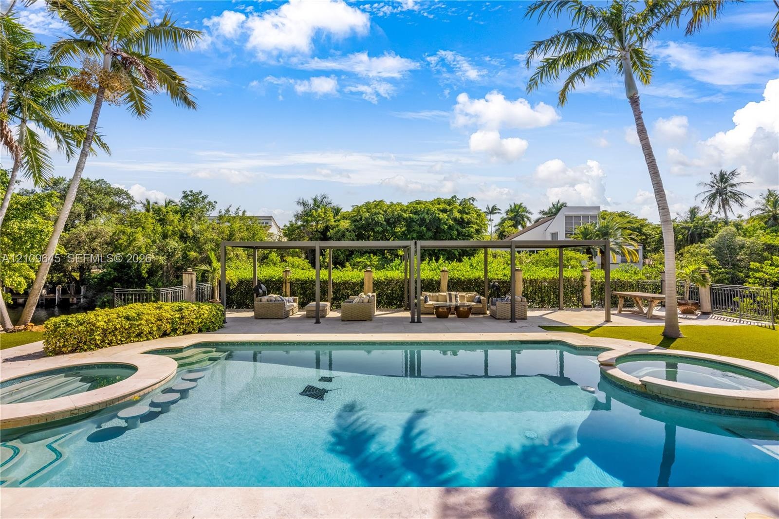 In-ground swimming pool with built-in wading stools and integrated spa, complemented by a stone-paved pool deck, covered pergola structure, and mature