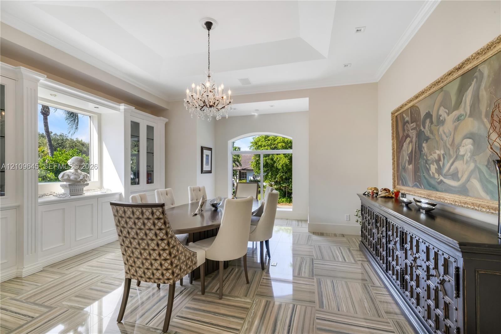 Tray ceiling featuring a central crystal chandelier, polished stone flooring, custom built-in cabinetry, and arched windows