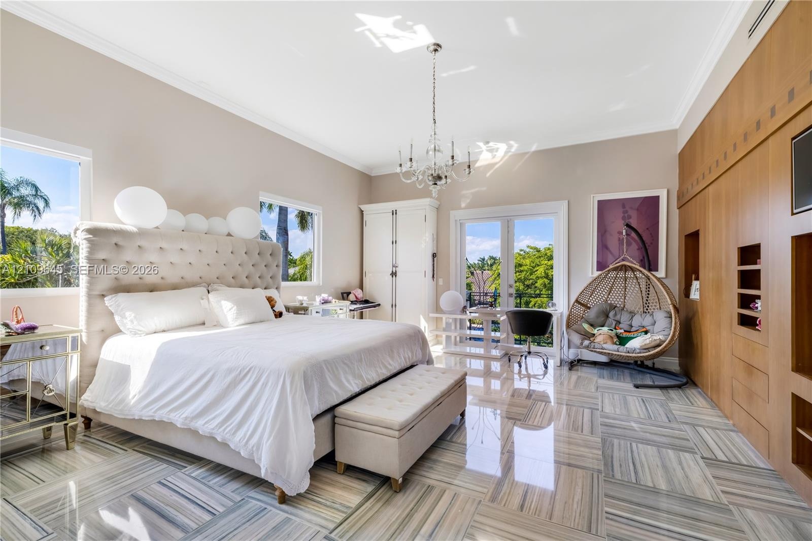 Polished natural stone flooring, custom floor-to-ceiling wood cabinetry, recessed crown molding, crystal chandelier, and French doors