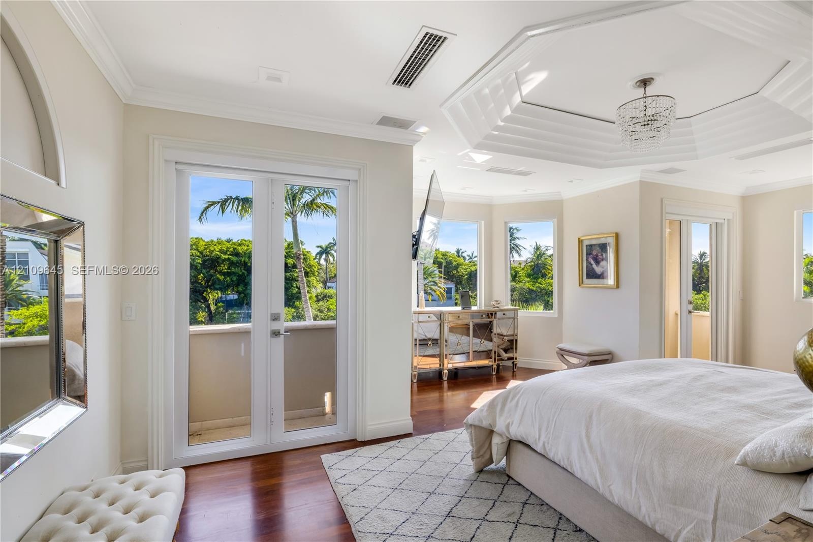 Octagonal tray ceiling with inset crown molding, polished wood-finish flooring, dual-pane glass entry doors, and multi-light crystal chandelier
