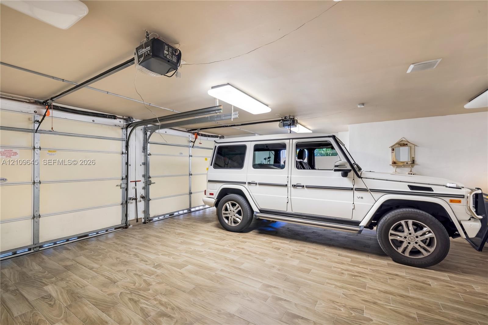 Garage featuring wood-finish flooring, dual motorized garage door openers, and rectangular LED light fixtures