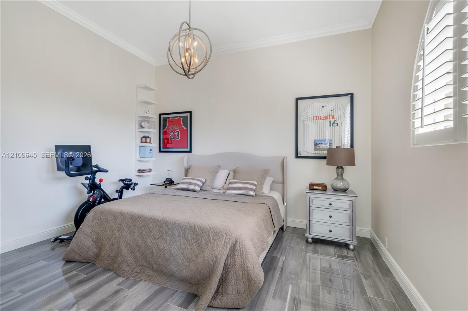 Room featuring wood-finish flooring, crown molding, a decorative orb chandelier, built-in shelving, and an arched window with plantation shutters