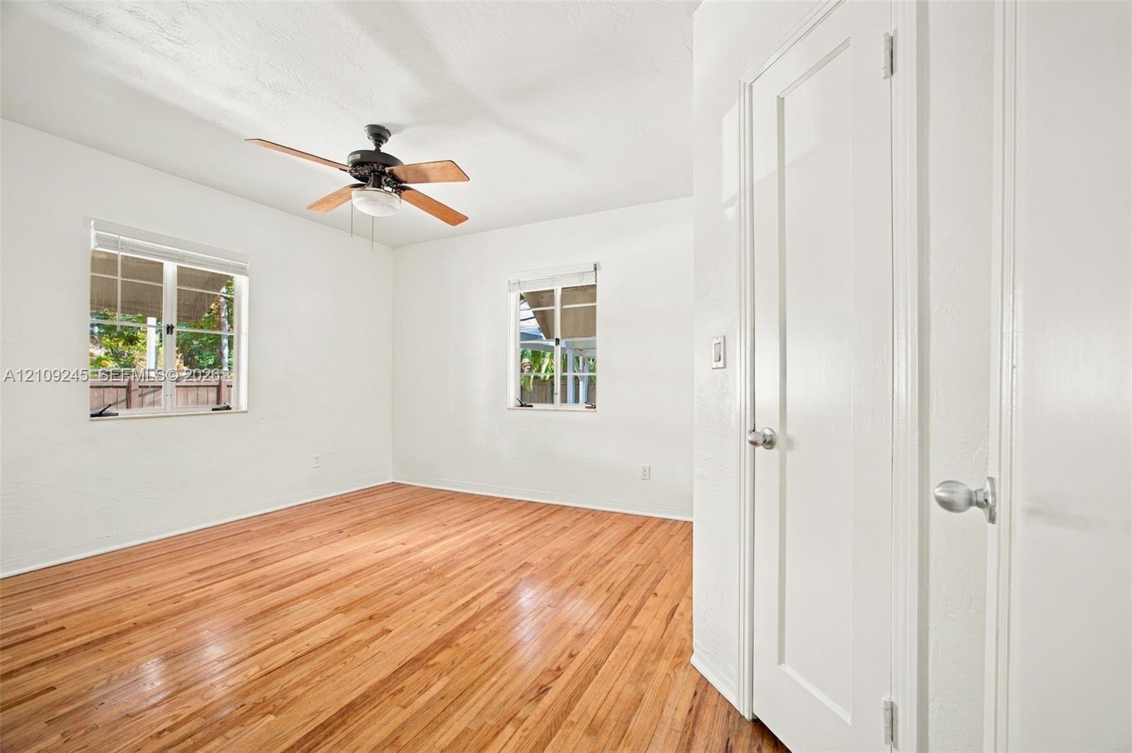 Interior room featuring wood-finish flooring, two windows with blinds, a ceiling fan with integrated lighting, and a white paneled door