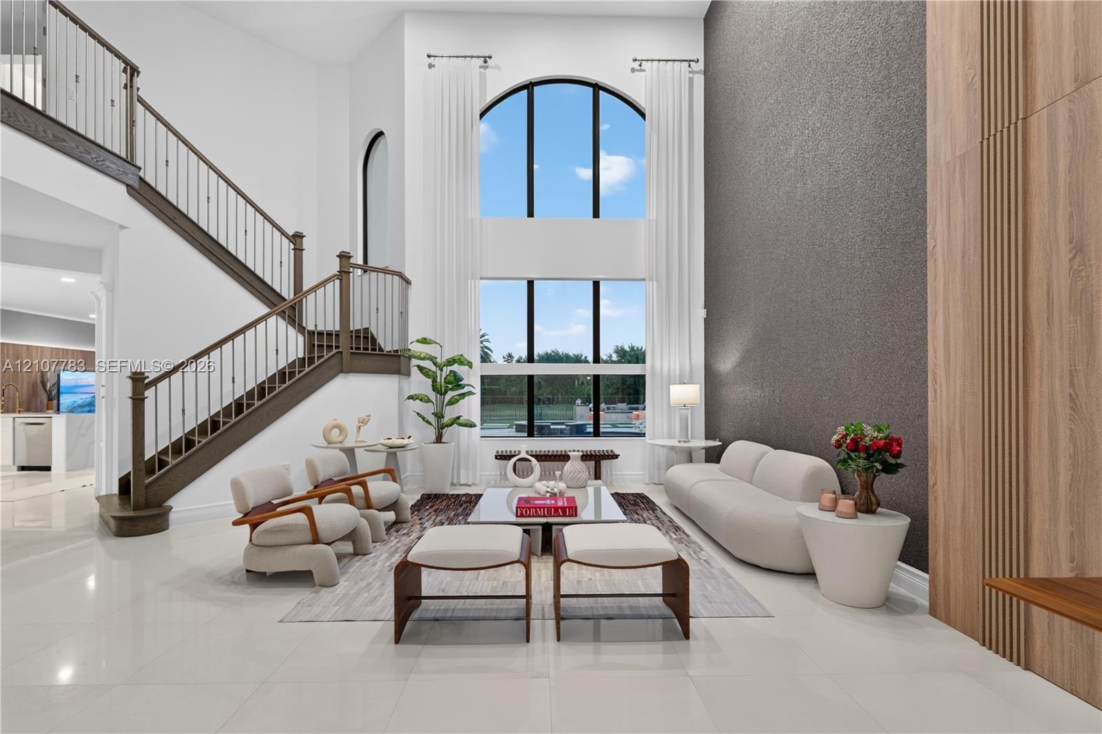 Two-story great room featuring a double-height arched window, floor-to-ceiling textured accent wall, wood-paneled wall detail, and a staircase with wr