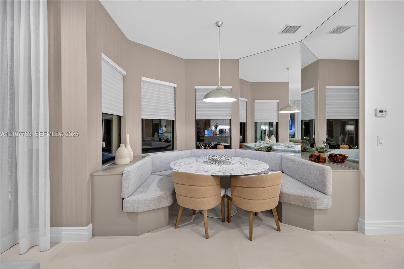 Custom built-in upholstered banquette seating, floor-to-ceiling wall mirror, bay window configuration with integrated blinds, and polished pendant lig