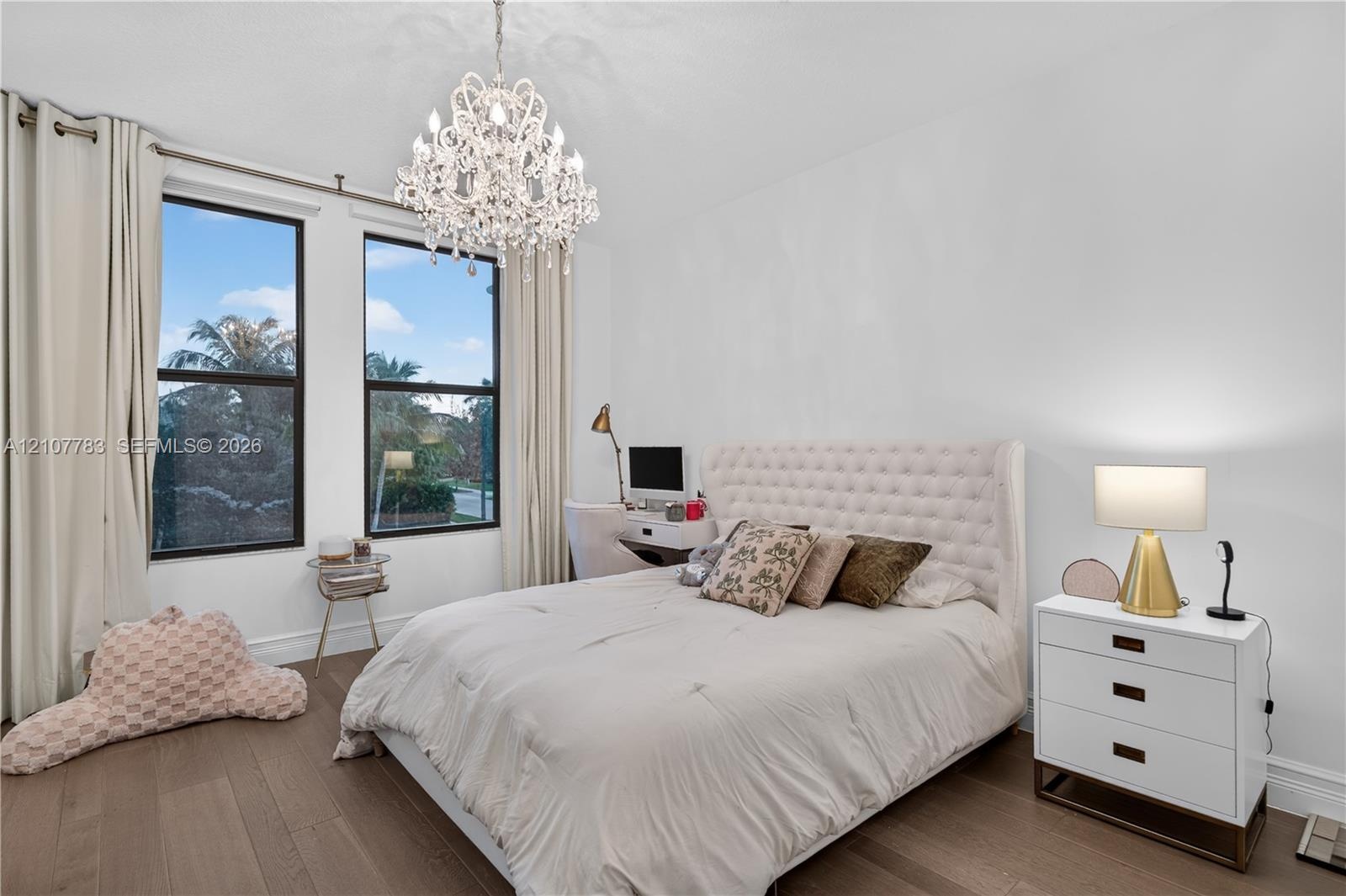 Room with wood-finish flooring, dual windows with dark frames, and a decorative crystal chandelier