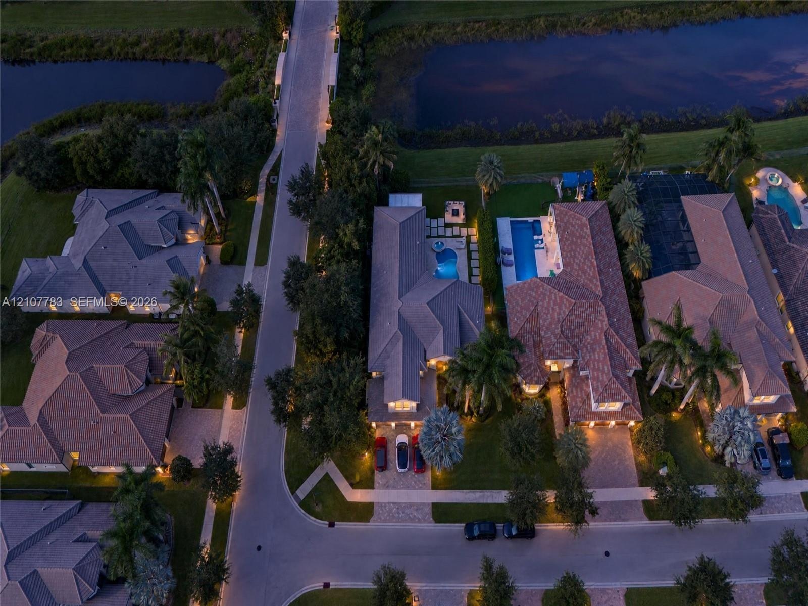 Aerial perspective of residential properties featuring tile roofing, paved driveways, private swimming pools, and landscaped perimeters situated along