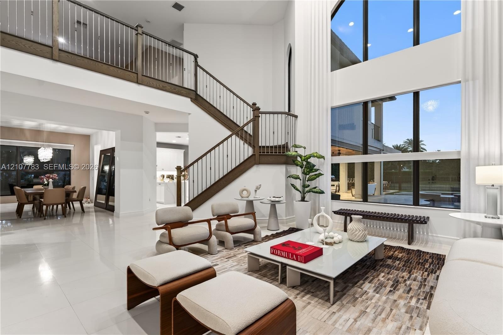 Two-story living area featuring floor-to-ceiling windows, porcelain tile flooring, and a grand staircase with wood-finished handrails and metal balust