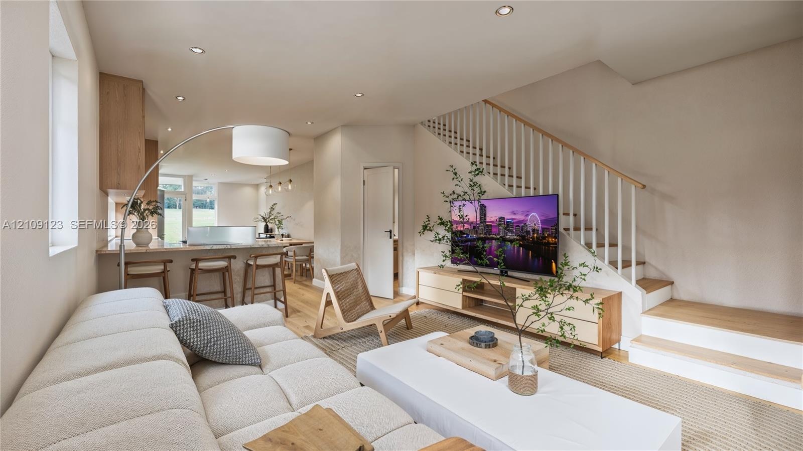 Open-concept interior featuring light wood-finish flooring, recessed lighting, a kitchen breakfast bar, and a staircase with white vertical balusters 