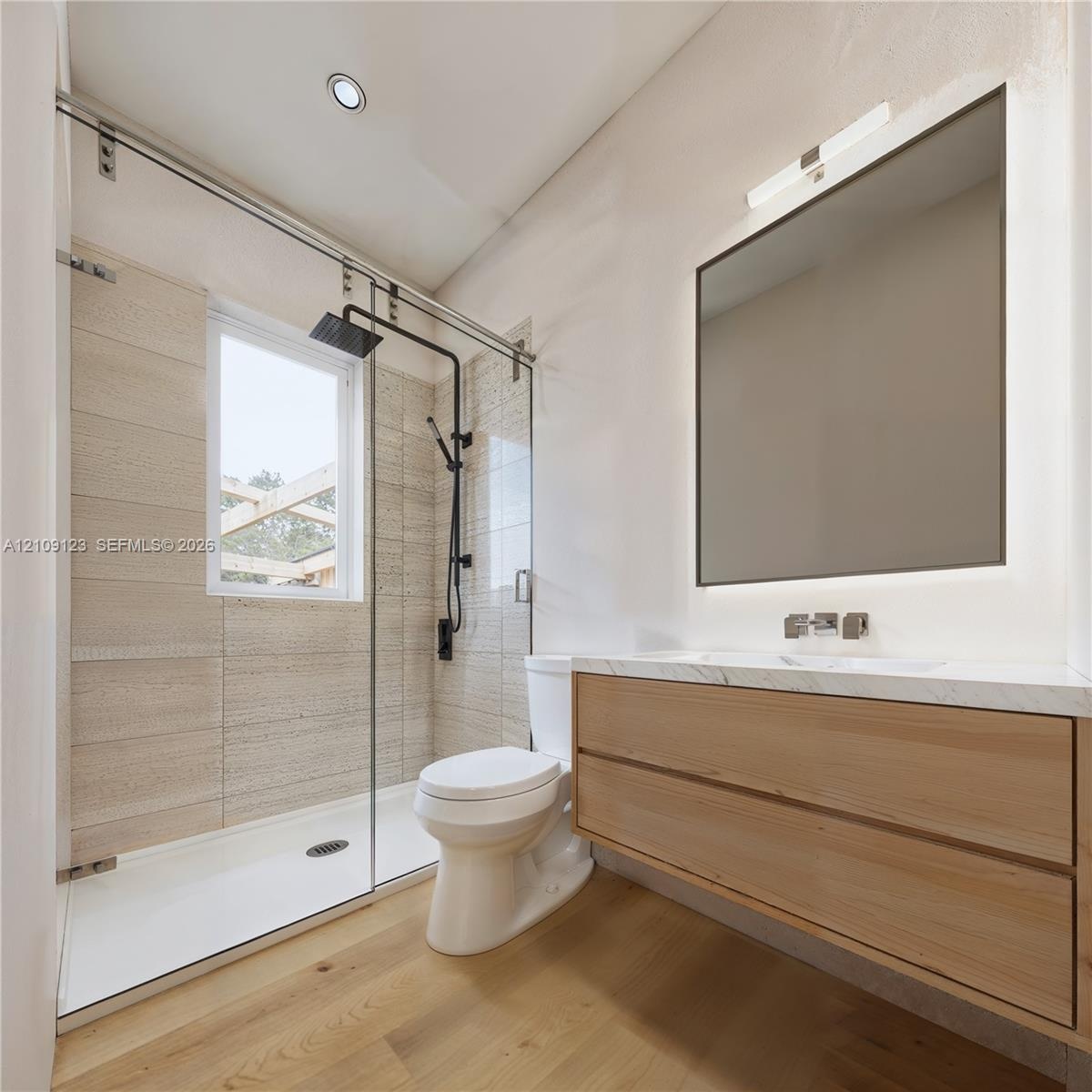 Floating wood-finish vanity with countertop, glass-enclosed shower with matte black fixtures, and recessed lighting