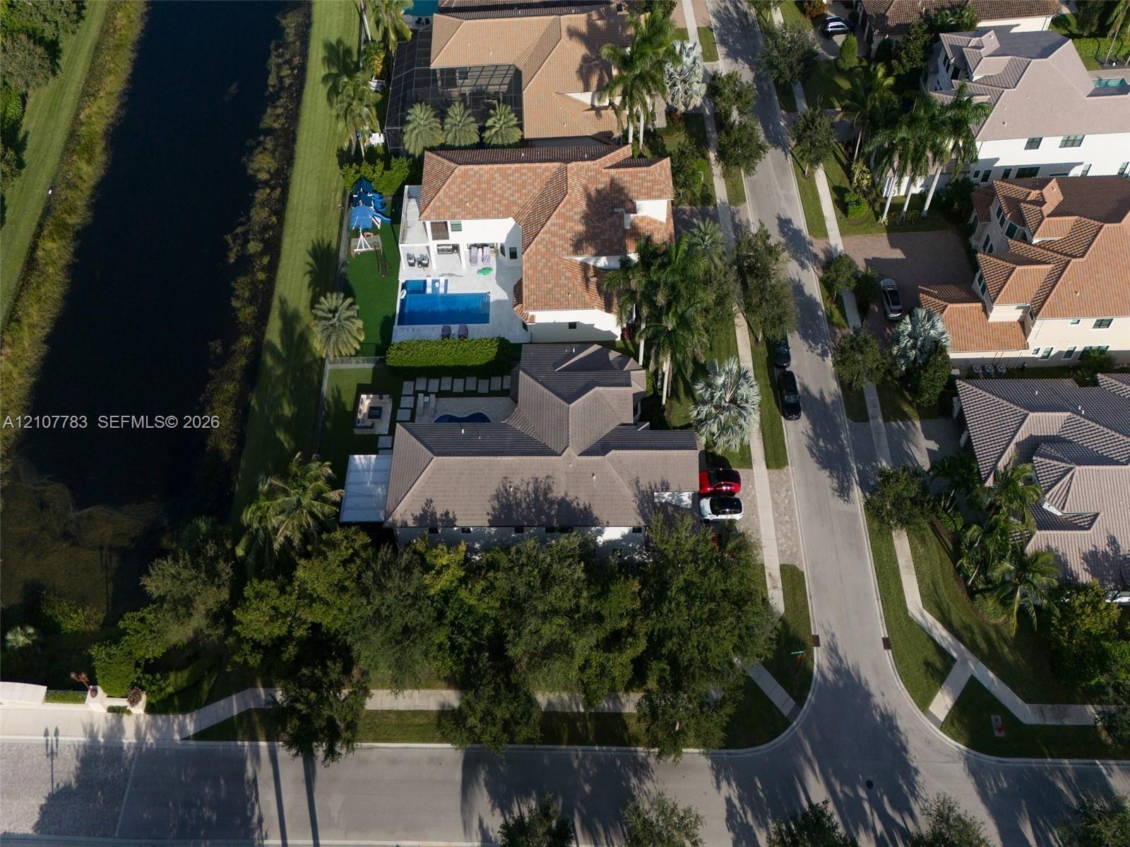 Aerial perspective of a waterfront property featuring a multi-pitched tiled roof, private swimming pool, concrete paver patio, and professional landsc