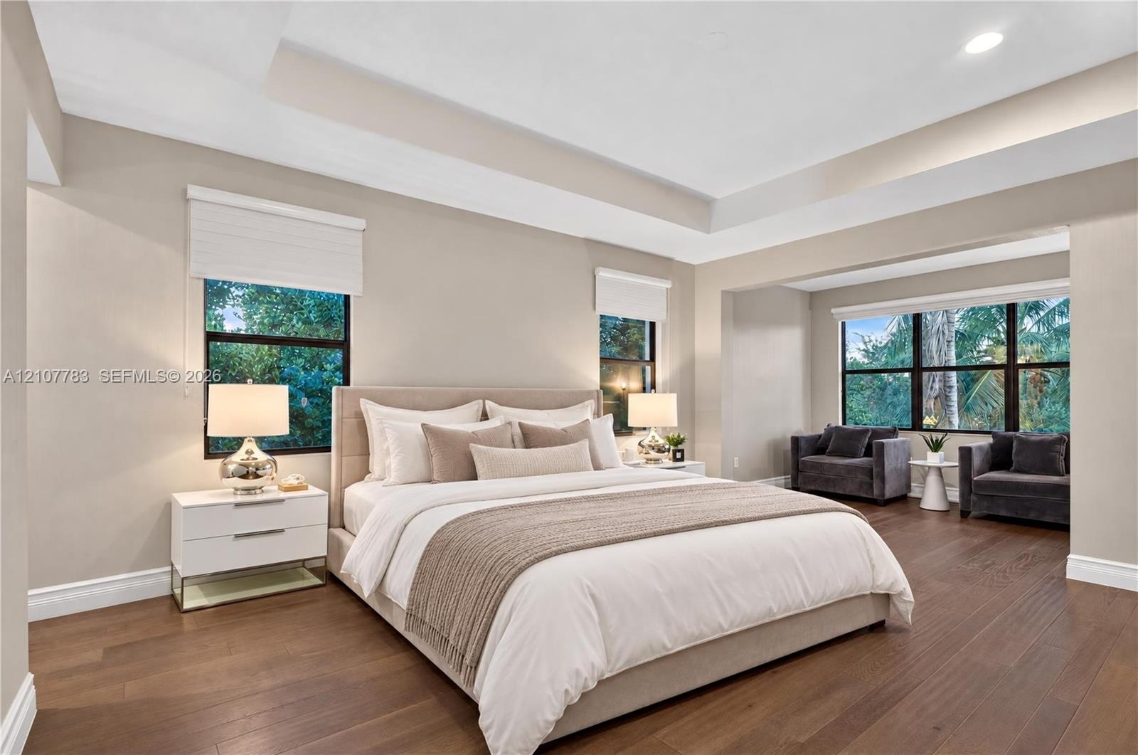 Bedroom featuring wood-finish flooring, a tiered tray ceiling, and multiple windows with roller shades