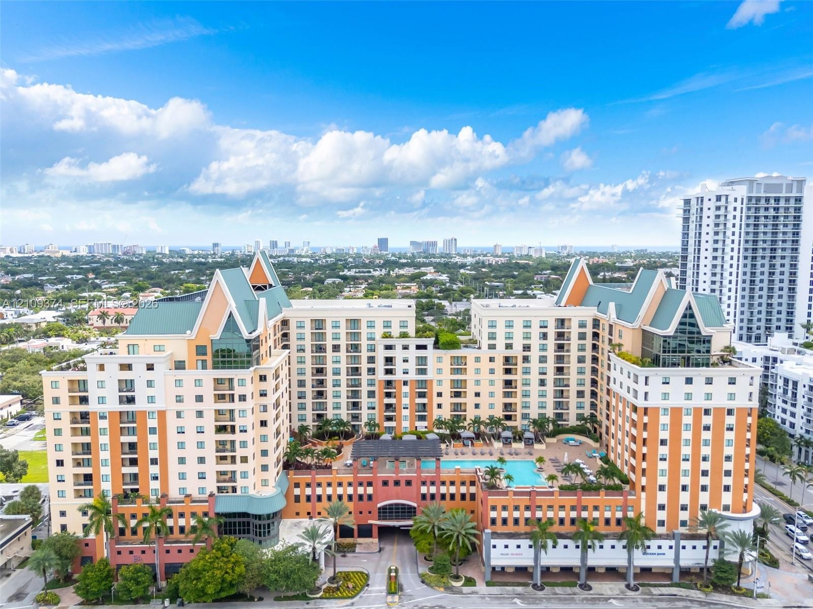 Multi-story high-rise building featuring a structured facade, gabled rooflines, recessed balconies, an elevated outdoor swimming pool, and manicured t
